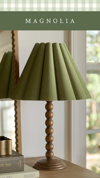 This image ad features an olive-green pleated lampshade atop a wooden table lamp from Magnolia, a home decor brand.