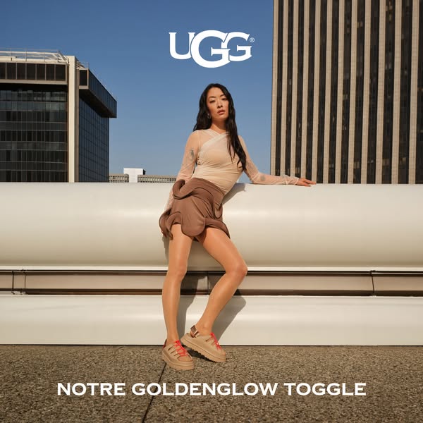 This ad features a person modeling the brand's new sandal. The model is leaning against a white rail with buildings