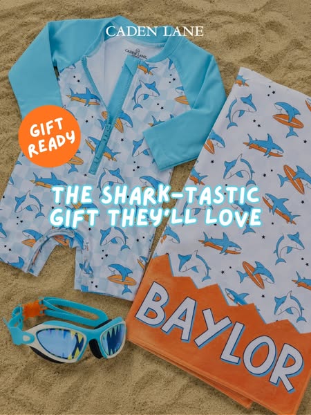 An ad for Caden Lane baby products. The products include a rash guard one piece bathing suit, beach towel, and goggles. 