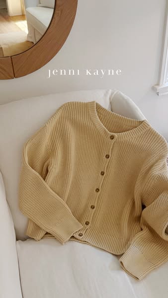 An image of a yellow cardigan is displayed on a white couch. A transparent brand logo overlays the top of the image.
