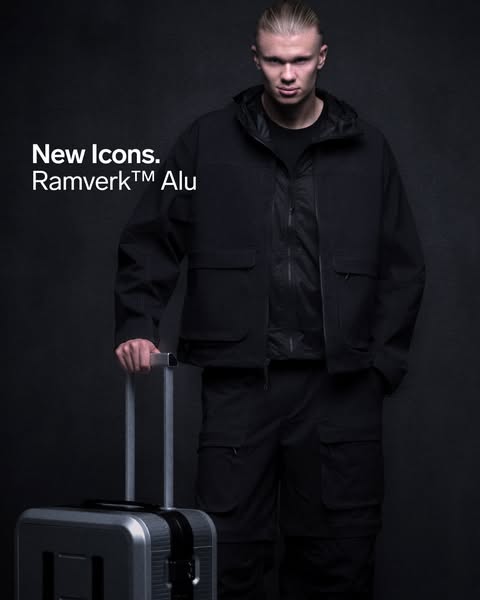 This image ad shows Erling Haaland, a professional soccer player, modeling a black jacket, pants, and carrying a suitcas