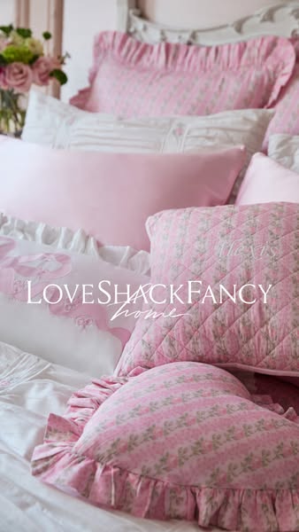 This LoveShackFancy ad showcases a bed with multiple pillows and bedding sets in their signature pink and floral style. 