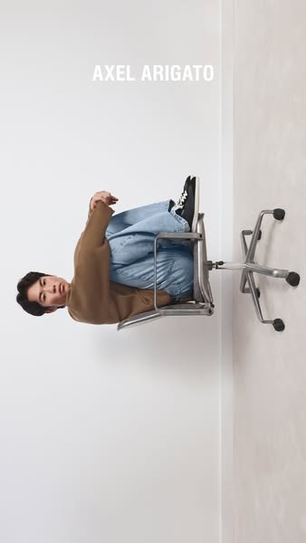 This ad features a person sitting sideways on a chair with the brand name 'AXEL ARIGATO' displayed above them. T