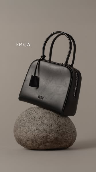 This image ad features a black Freja handbag positioned on top of a grey stone. The ad highlights the product's mate