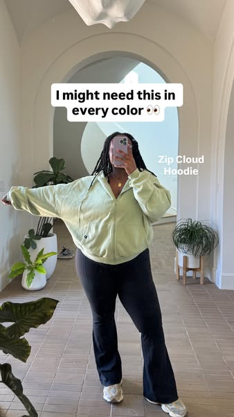 A creator selfie-style image ad features a woman wearing a light green zip up hoodie and black yoga pants, standing in a