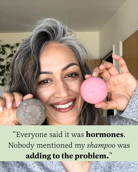 An image ad featuring a woman holding a pink shampoo bar and a gray conditioner bar. She is smiling and looking directly