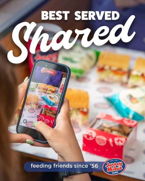 This Jersey Mike's image ad features a person taking a photo of Jersey Mike's subs and snacks on a table using t