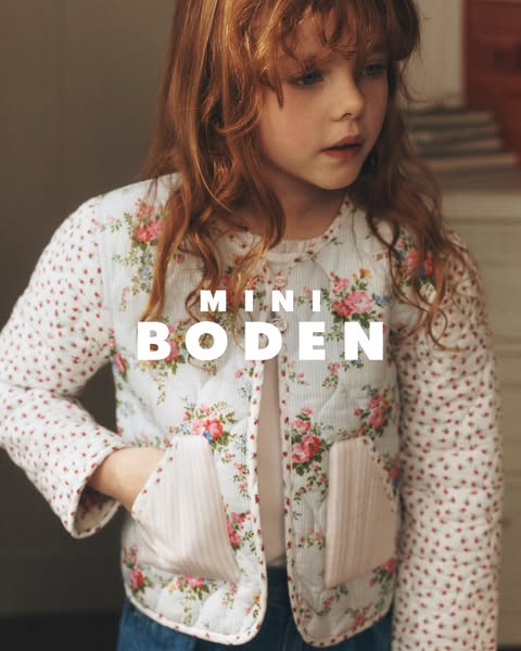 A young child is wearing a quilted jacket from Mini Boden. The jacket is white with a floral pattern on the body and a p