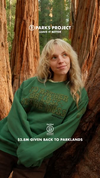 An image ad featuring a woman wearing a green Parks Project sweatshirt in a forest. The ad highlights the brand's co