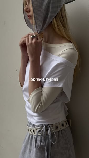 This ad features a woman modeling a beige long sleeve shirt layered under a white t-shirt. She is also wearing a gray he