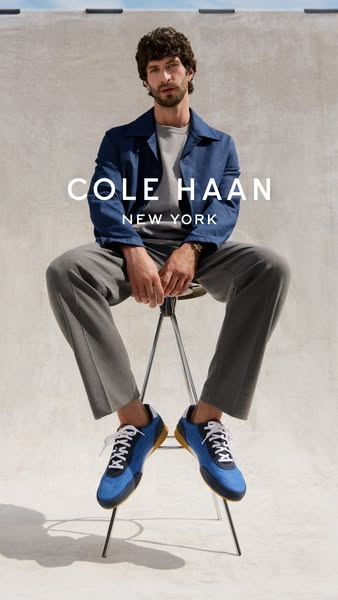 A male model is shown seated in front of a neutral background, wearing a navy jacket, grey shirt and pants, and blue Col