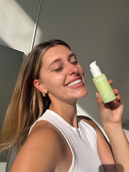 This ad features a woman holding and smiling at a bottle of Hey Bud's Good Vibrations Facial Oil. It is a selfie-sty