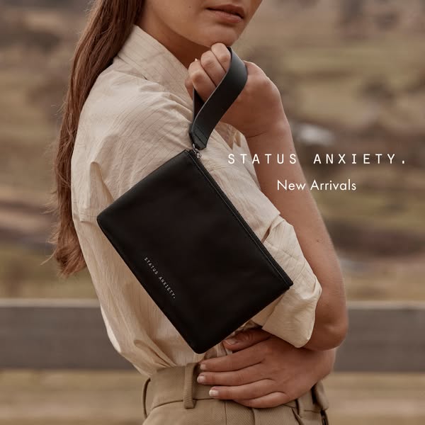 This image ad features a black Status Anxiety clutch bag and promotes new arrivals. The ad showcases a woman holding the