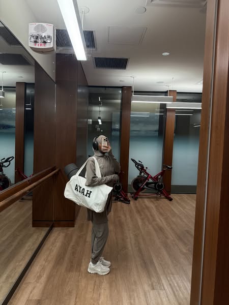 This ad features a woman in a matching athletic outfit with a handbag that says 'Ayah' on it. She stands in a gy