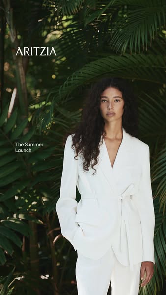 This Aritzia ad showcases a model wearing a white blazer and pants from their summer collection against a lush, tropical