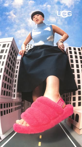 This ad features a woman with her foot in a pink UGG slide standing on an illustration of a street. She appears to be gi