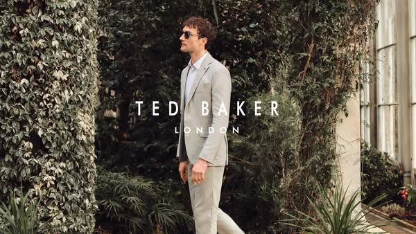 This image ad showcases a man wearing a light gray Ted Baker suit while walking through a garden.