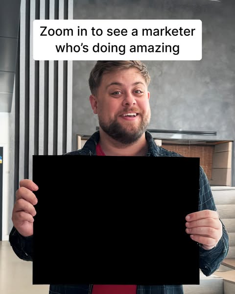 This ad shows a man holding a blank black sign, and tells viewers to zoom in to see a marketer who's doing amazing.
