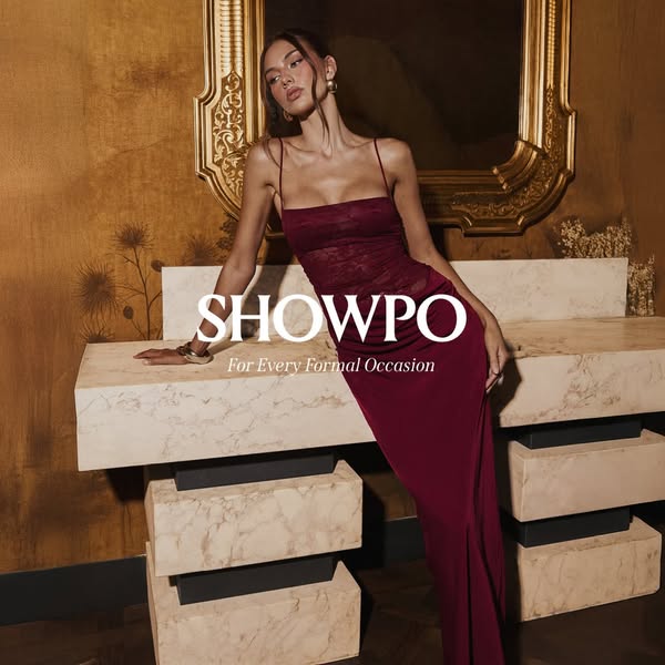 This Showpo ad features a young woman modeling a formal dress in a staged, high-fashion style setting. The focal point i