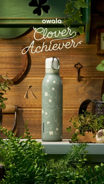 This ad showcases the Owala water bottle in the Clover Achiever design. The ad uses a natural, earthy aesthetic with pla