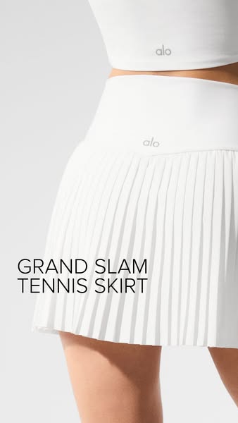 This image ad showcases the Alo Yoga 'Grand Slam' tennis skirt on a model. It highlights the product's desig