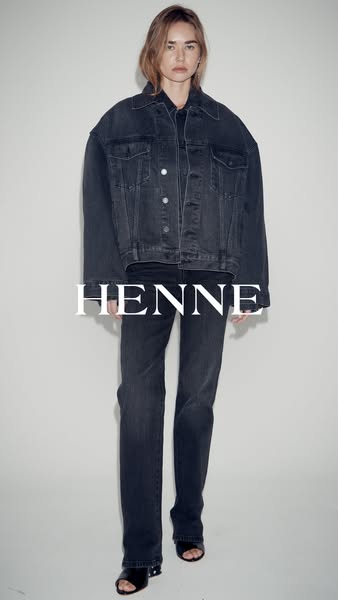 A woman poses wearing a denim jacket and jeans.