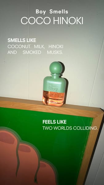 An image ad for Boy Smells Coco Hinoki fragrance. The ad features the product placed on a wooden surface with a painting
