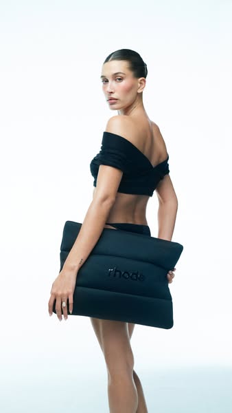 This ad features Hailey Bieber showcasing the Rhode brand while holding a black Rhode Pouch.