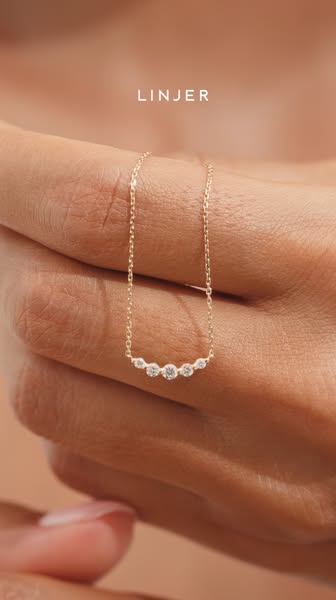 This ad features a close-up of a delicate gold necklace with small diamonds being held by a hand. The brand name, LINJER