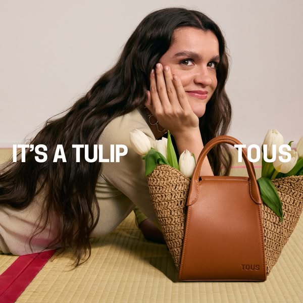 A woman is lying on a mat with a tan leather and straw tote bag beside her. The ad has the brand name and the tagline
