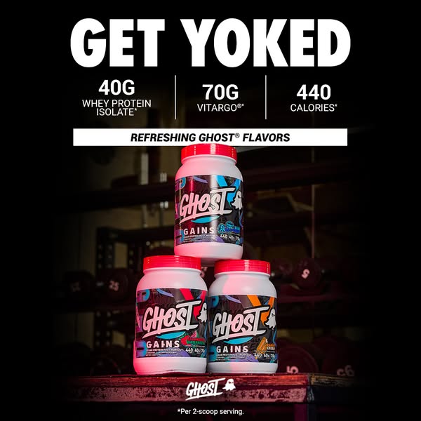 The image ad showcases three tubs of Ghost Gains protein powder stacked on a wooden surface in front of a gym setting. T
