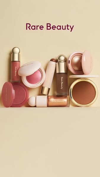 This image ad features a collection of Rare Beauty complexion products artfully arranged on a pale yellow background, sh