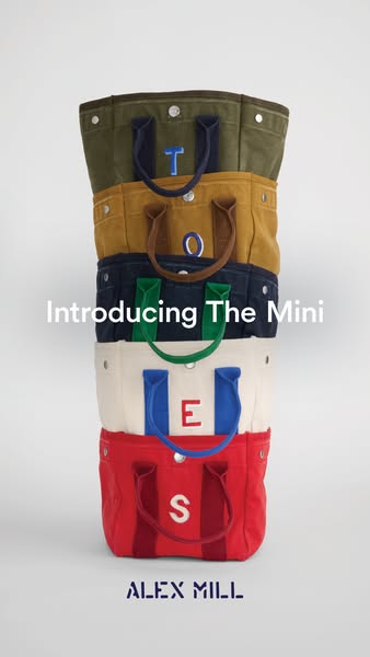This ad displays a stack of The Mini totes from Alex Mill, each of a different color, to advertise the bag.