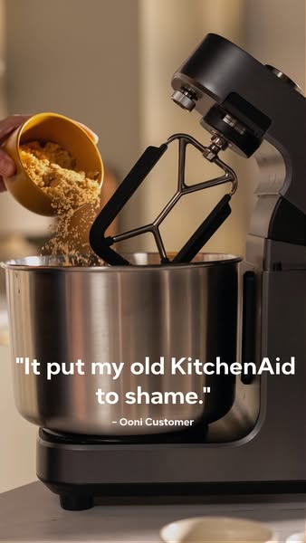This ad features a close-up of an Ooni stand mixer as someone pours brown sugar into its stainless steel bowl. A testimo