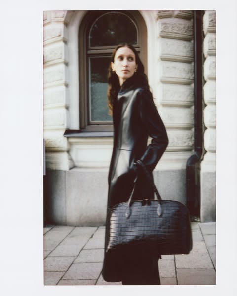 This ad features a woman in a dark dress and gloves holding a black bag. The ad has a white border similar to a polaroid