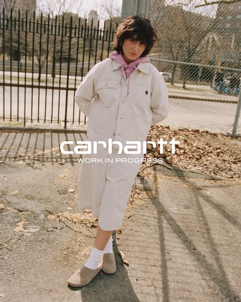 An ad showcasing Carhartt apparel, featuring a model in an outdoor setting wearing a matching jacket and skirt set.