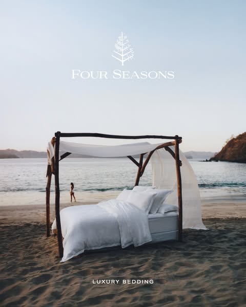 This image ad for Four Seasons promotes their luxury bedding. The ad features a bed with white linens set up on a beach,