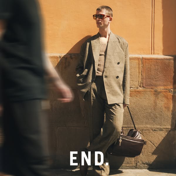 This ad features a man leaning against a textured wall, showcasing a neutral-toned outfit from END. The composition emph