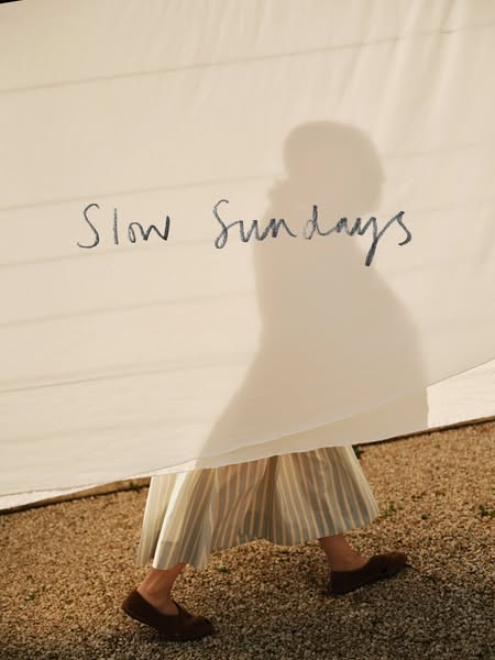 An image ad promoting the idea of 'slow Sundays' that shows a woman in a skirt and shoes standing in a gravel se