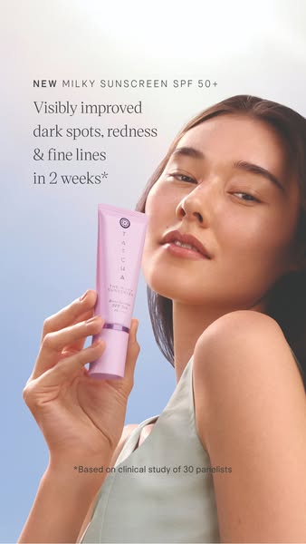 A skincare advertisement showcasing Tatcha's new Milky Sunscreen SPF 50+. The ad features a woman holding the produc