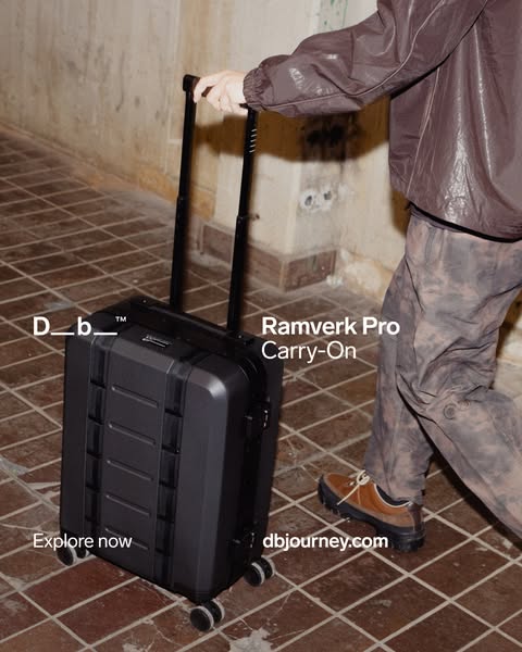 The ad features a Db Ramverk Pro Carry-On suitcase with a person pulling it on a tiled floor. The ad emphasizes the Db b