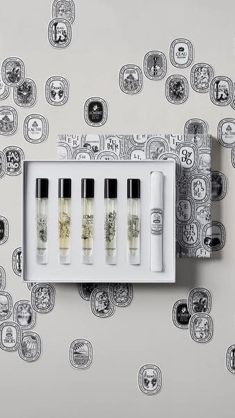 This ad showcases a Diptyque perfume set in a box. The fragrances come in small clear bottles with black tops. The box i