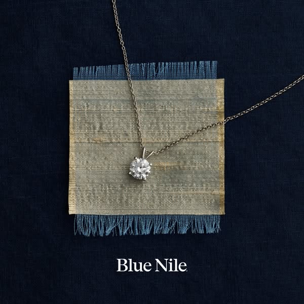 This ad for Blue Nile features a solitaire diamond pendant necklace against a textured blue background.