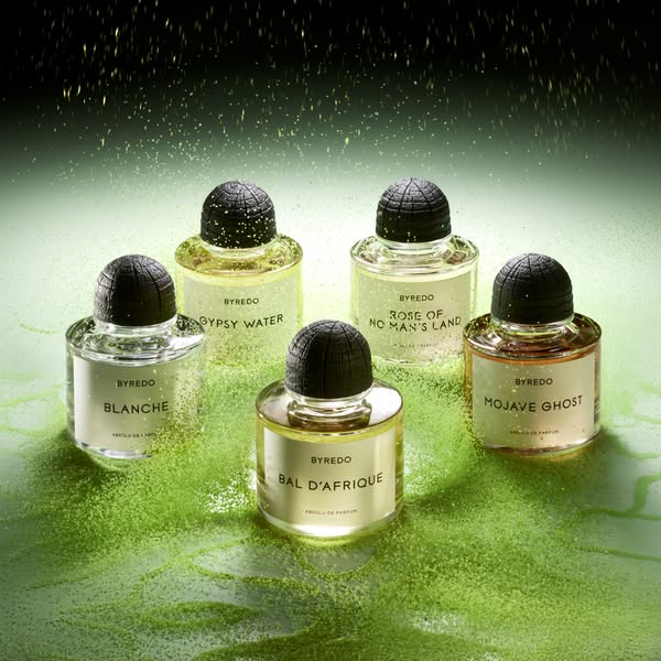 This ad features five perfume bottles from Byredo, all with different scents, displayed on a green glittery surface, hig