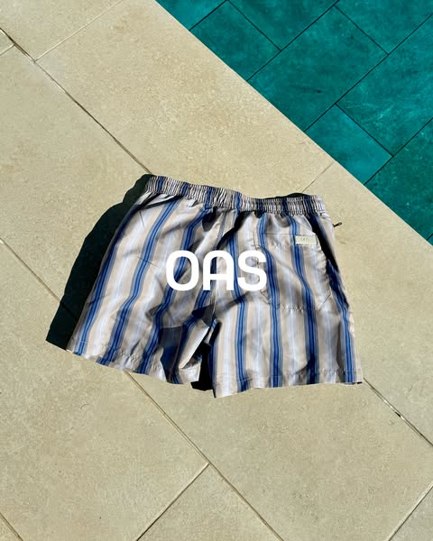 An image ad featuring a pair of OAS striped swim trunks next to a pool, which may connote that the brand is associated w