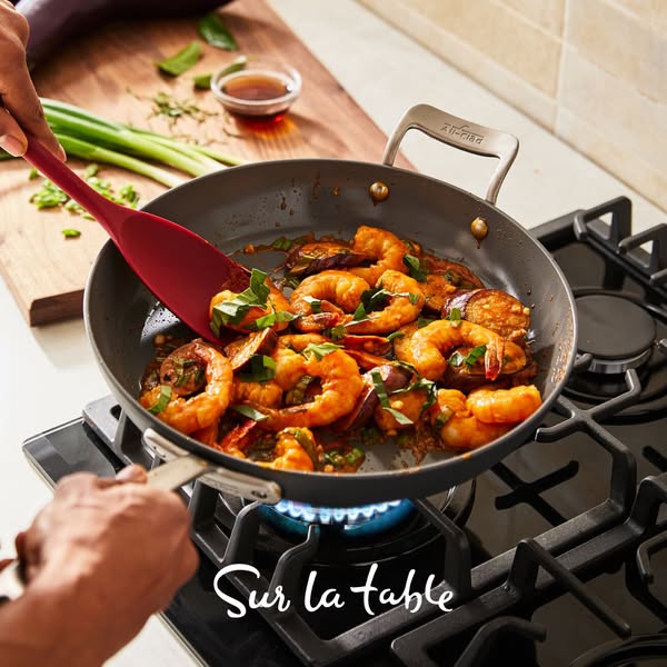 This image showcases a shrimp and eggplant stir-fry being cooked in an All-Clad pan. The ad also features the logo for t