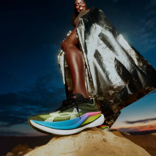 This is a product ad showcasing a running shoe. A model is standing on a rock wearing the shoe.