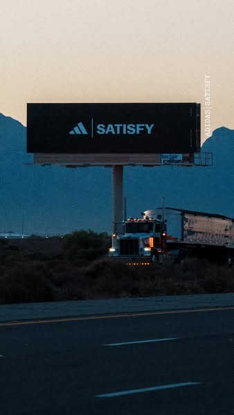 This ad shows a billboard on the side of the road featuring the Adidas and Satisfy logos to announce their partnership.