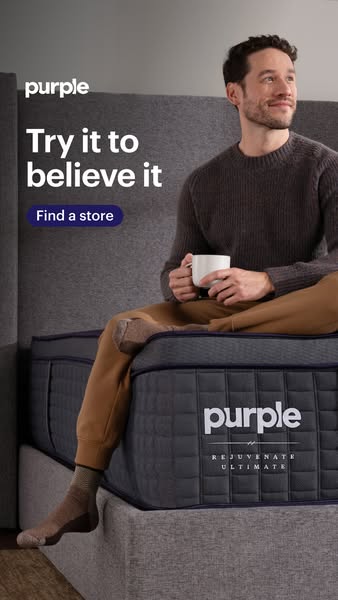 A man is sitting on a Purple Rejuvenate Ultimate mattress while holding a mug.