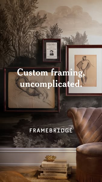 This image ad for Framebridge features a close-up shot of framed art pieces hanging on a wall, above a stack of books an